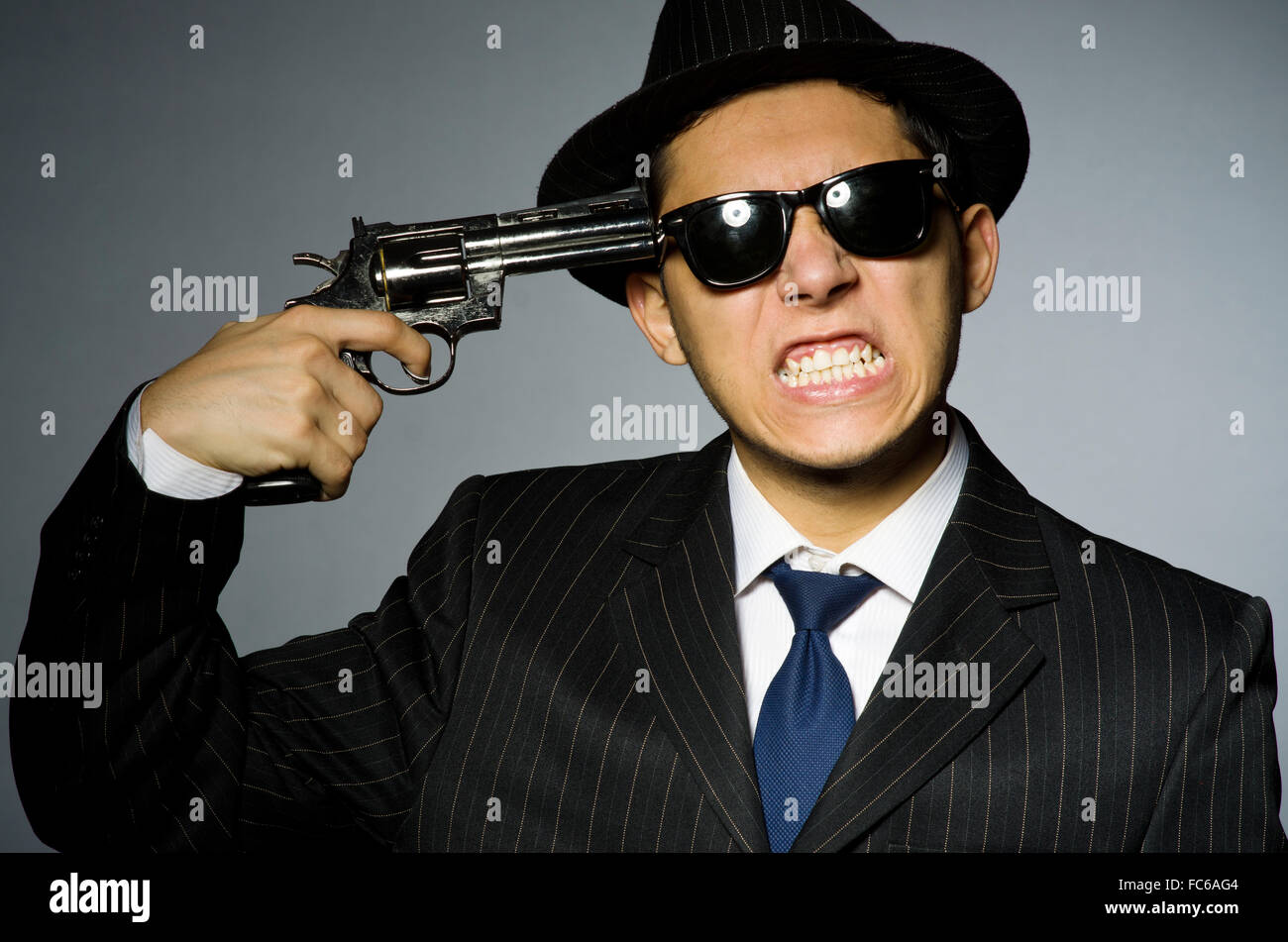 Young man in elegant suit holding handgun against gray Stock Photo