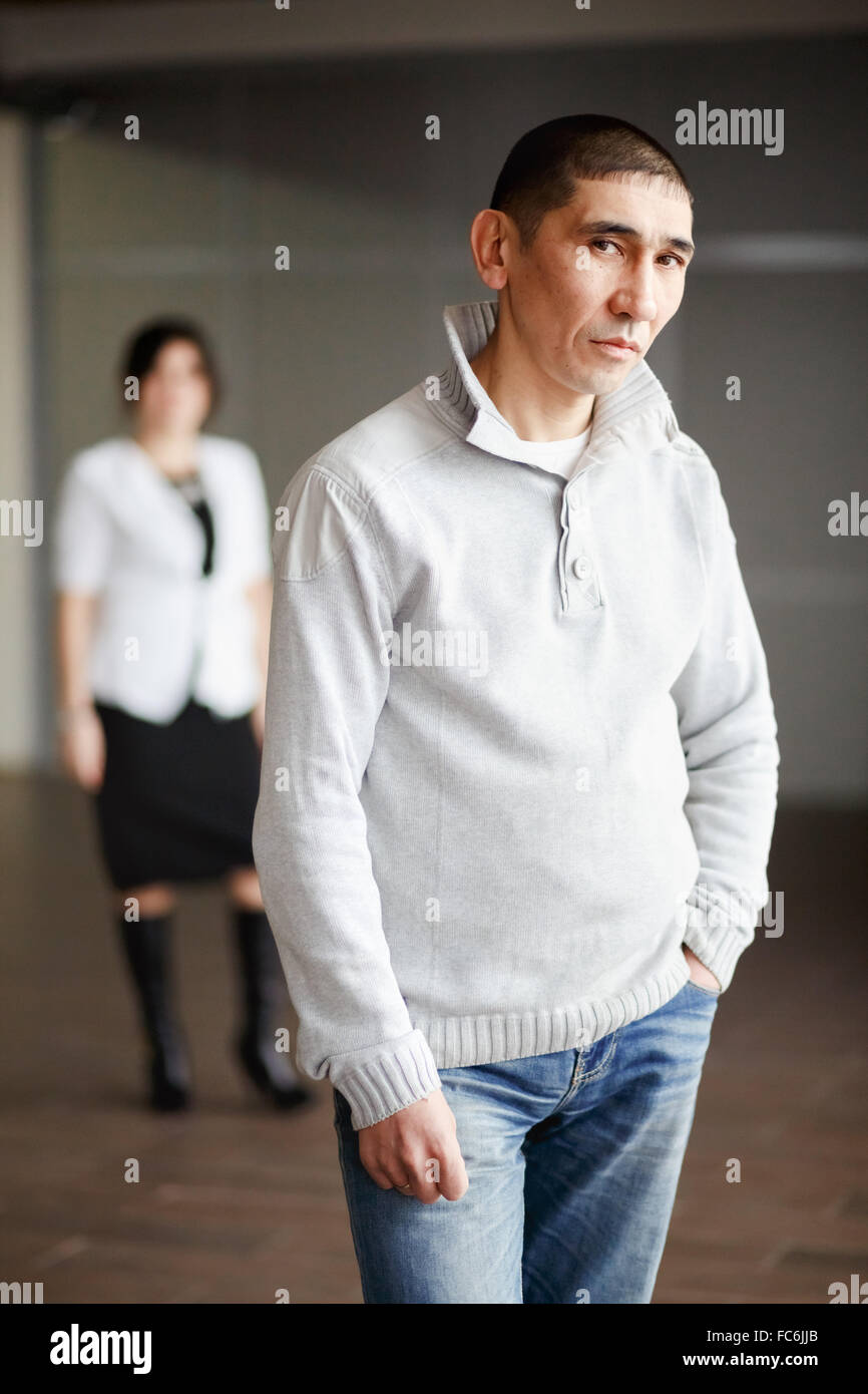 Middle aged man in casual clothes with short hair thoughtfully looking directly into camera, the employee gets job. In background, HR Director woman wearing white suit and strict black dress waits. Stock Photo