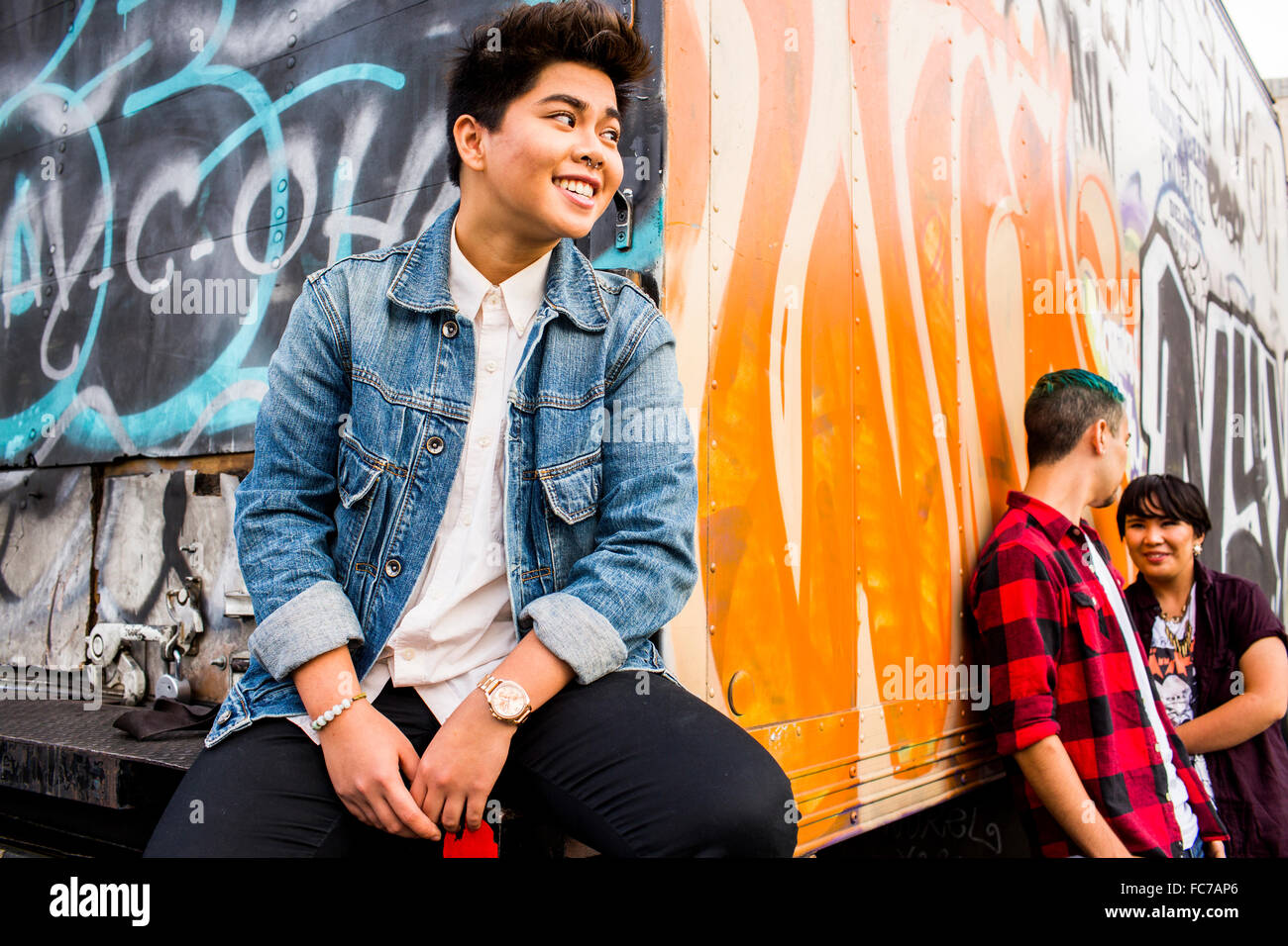 Woman listening to friends talking at graffiti truck Stock Photo