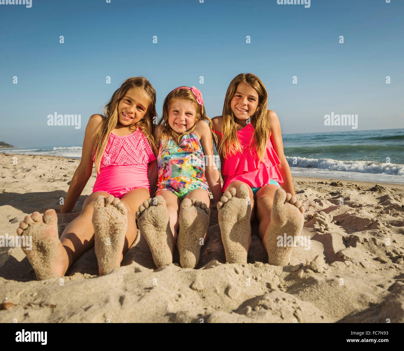 Caucasian sisters with sandy feet on beach Stock Photo