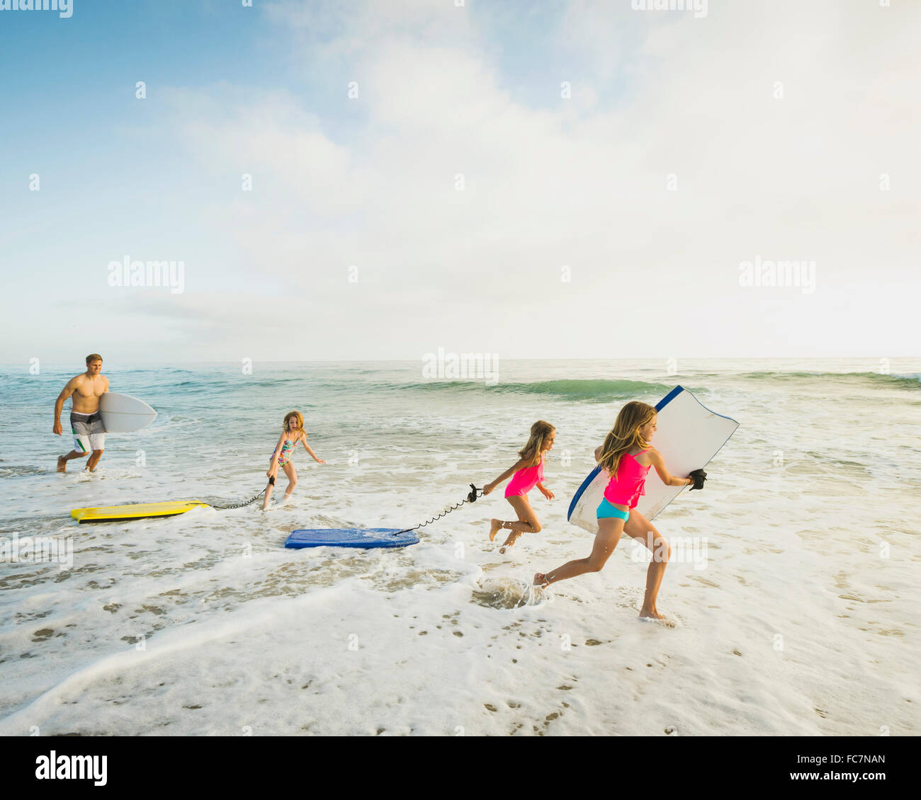 Caucasian father and daughters playing in waves on beach Stock Photo