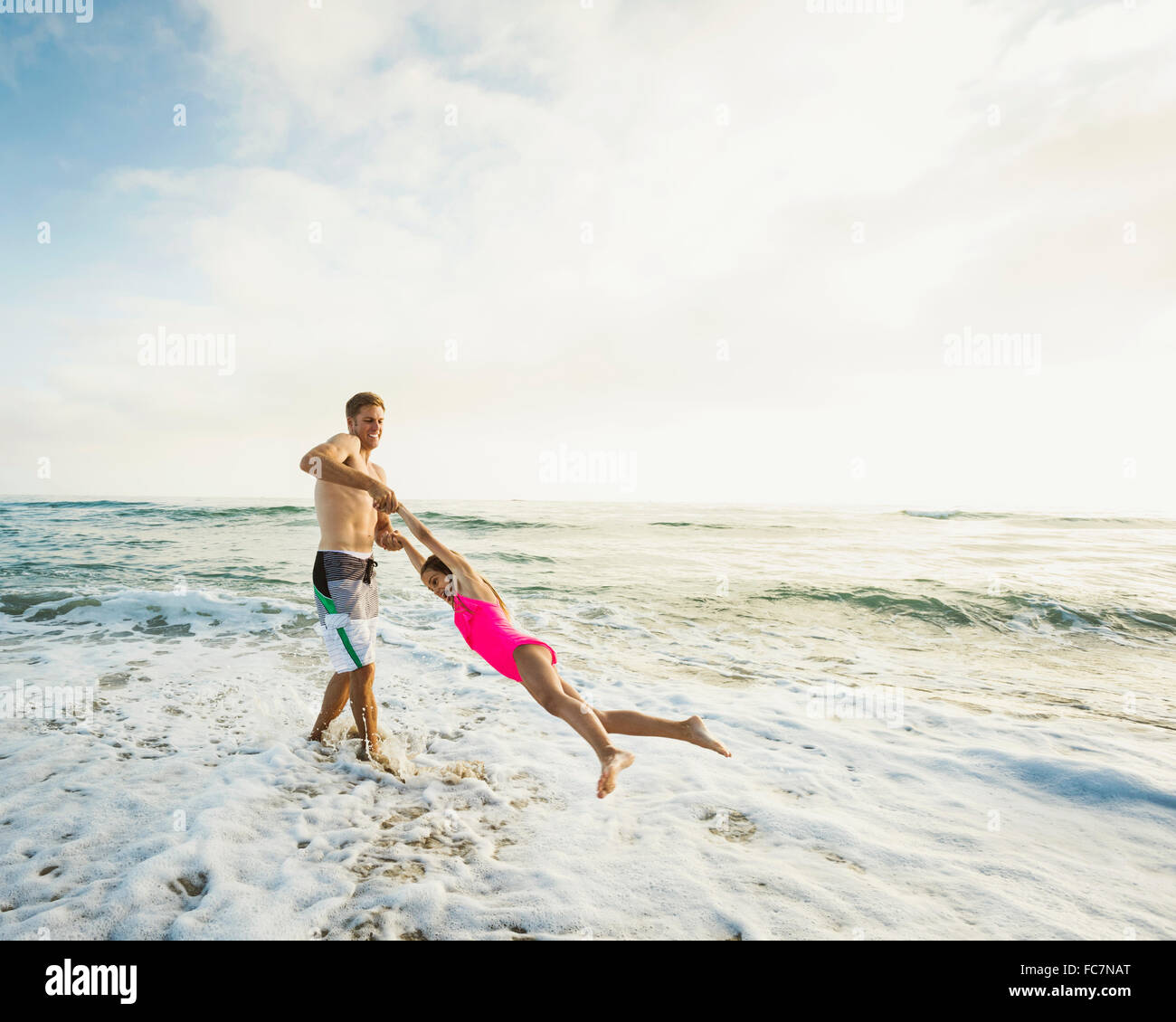 Caucasian father and daughter playing in waves on beach Stock Photo