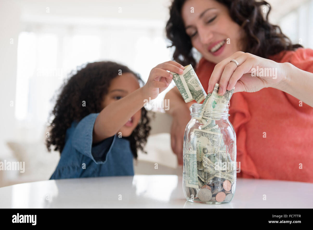 Mother and daughter saving money in jar Stock Photo - Alamy
