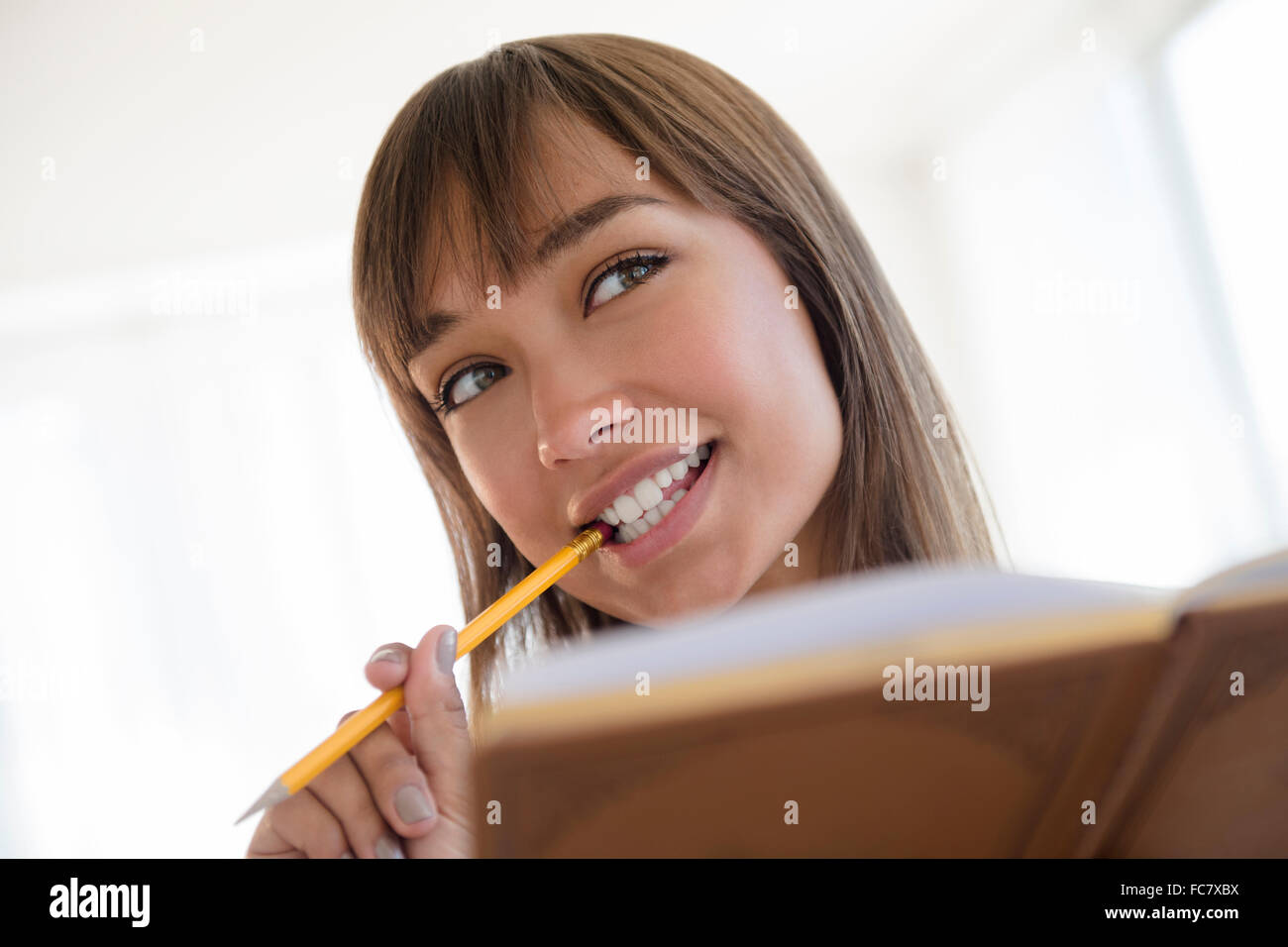 Mixed race woman chewing pencil and reading Stock Photo