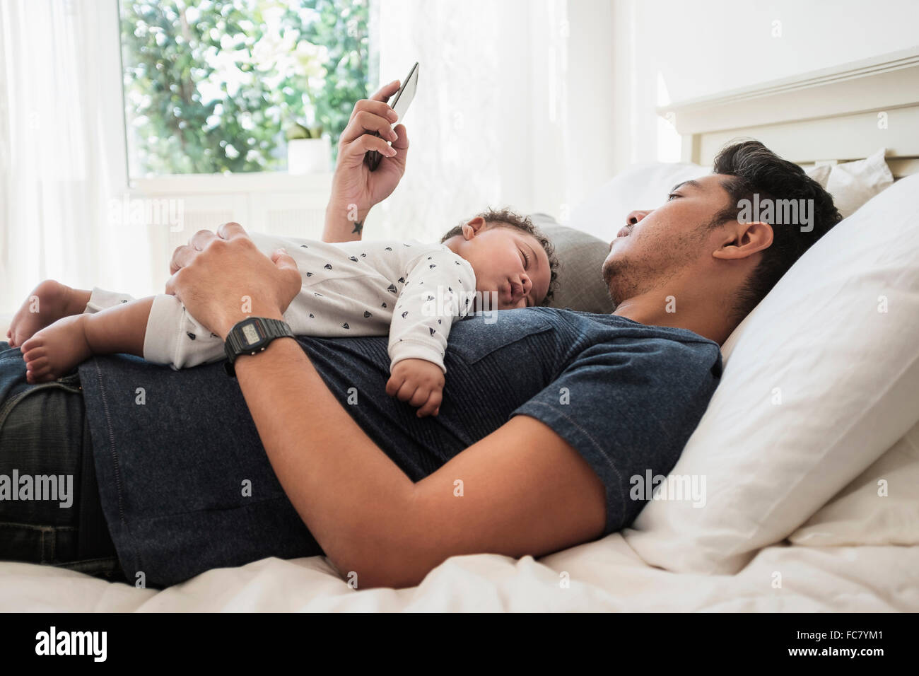 Father using cell phone with sleeping baby son Stock Photo