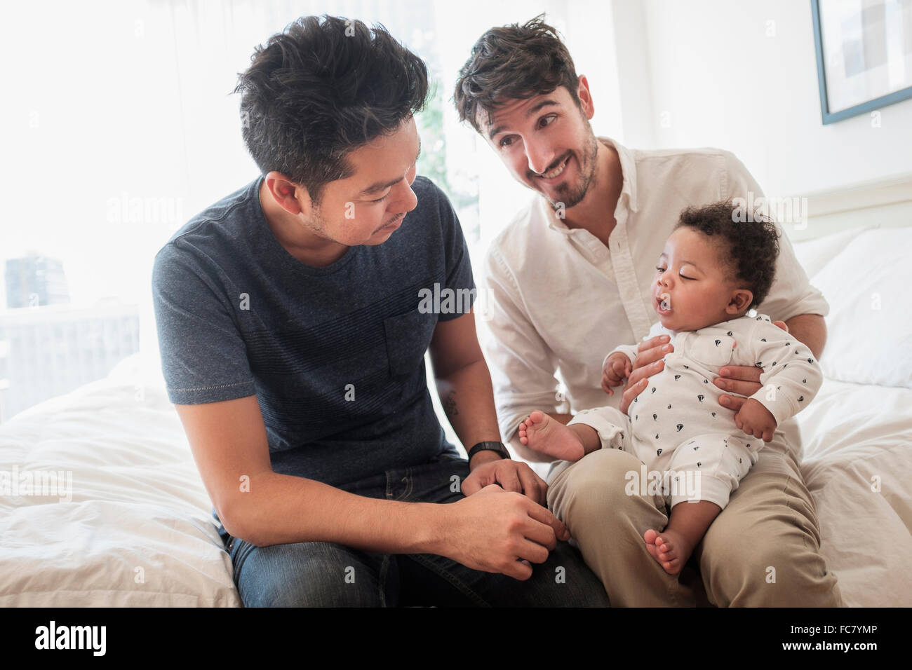 Gay fathers playing with baby son on bed Stock Photo