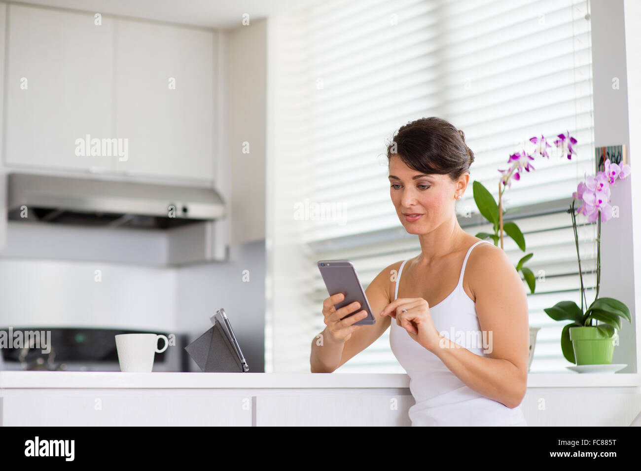 Caucasian woman using cell phone in kitchen Stock Photo