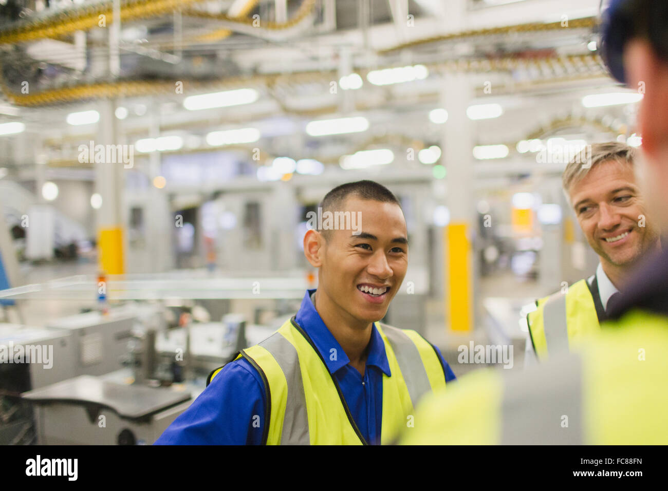 Workers in reflective clothing talking in factory Stock Photo