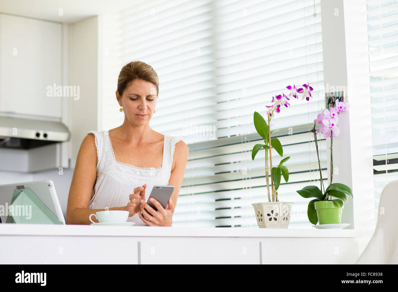 Caucasian woman using cell phone in kitchen Stock Photo