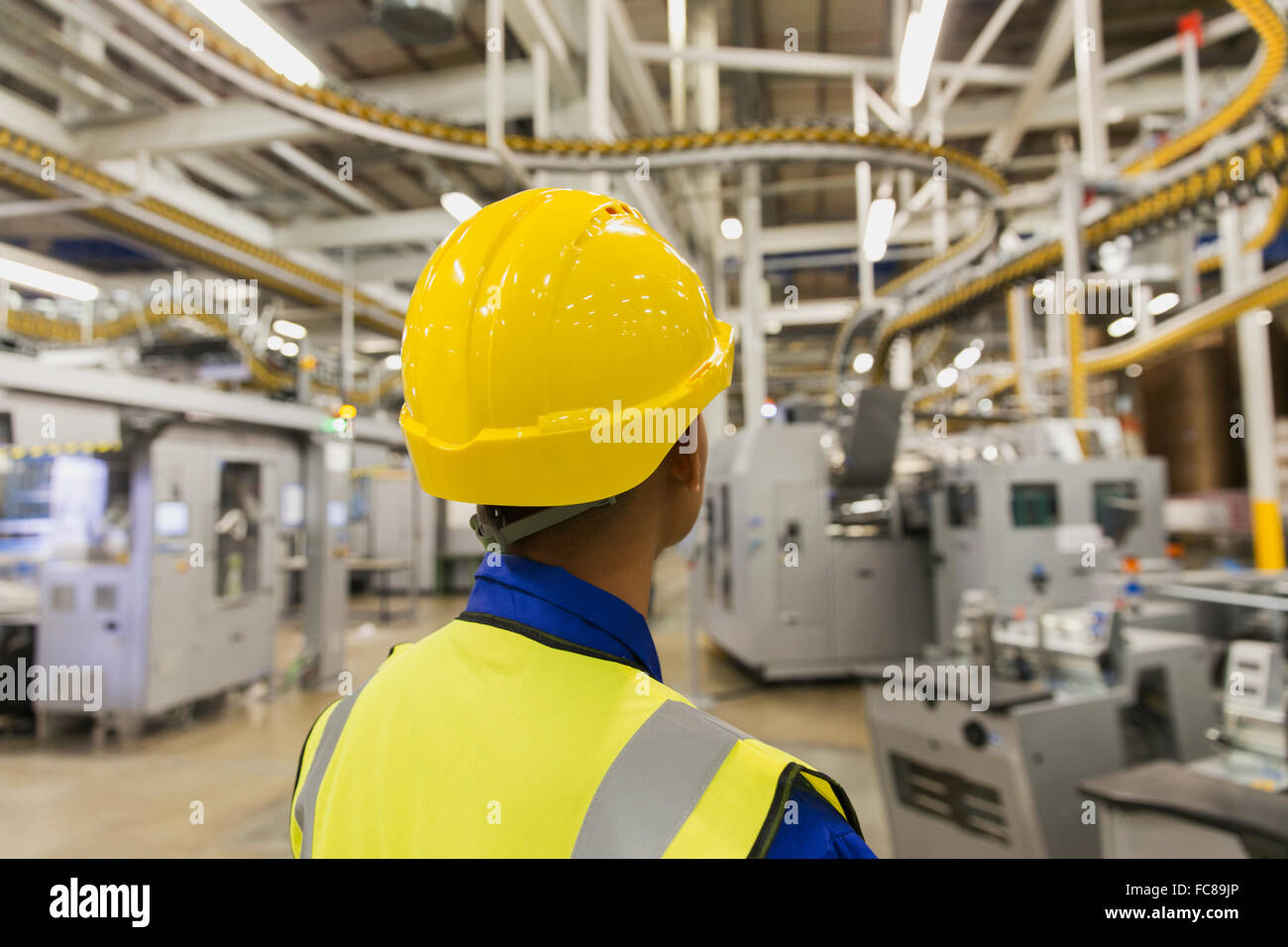 Worker in hard-hat watching printing press conveyor belts and machinery in printing plant Stock Photo