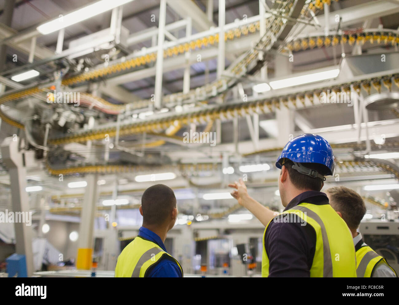 Workers discussing winding printing press conveyor belts overhead Stock Photo