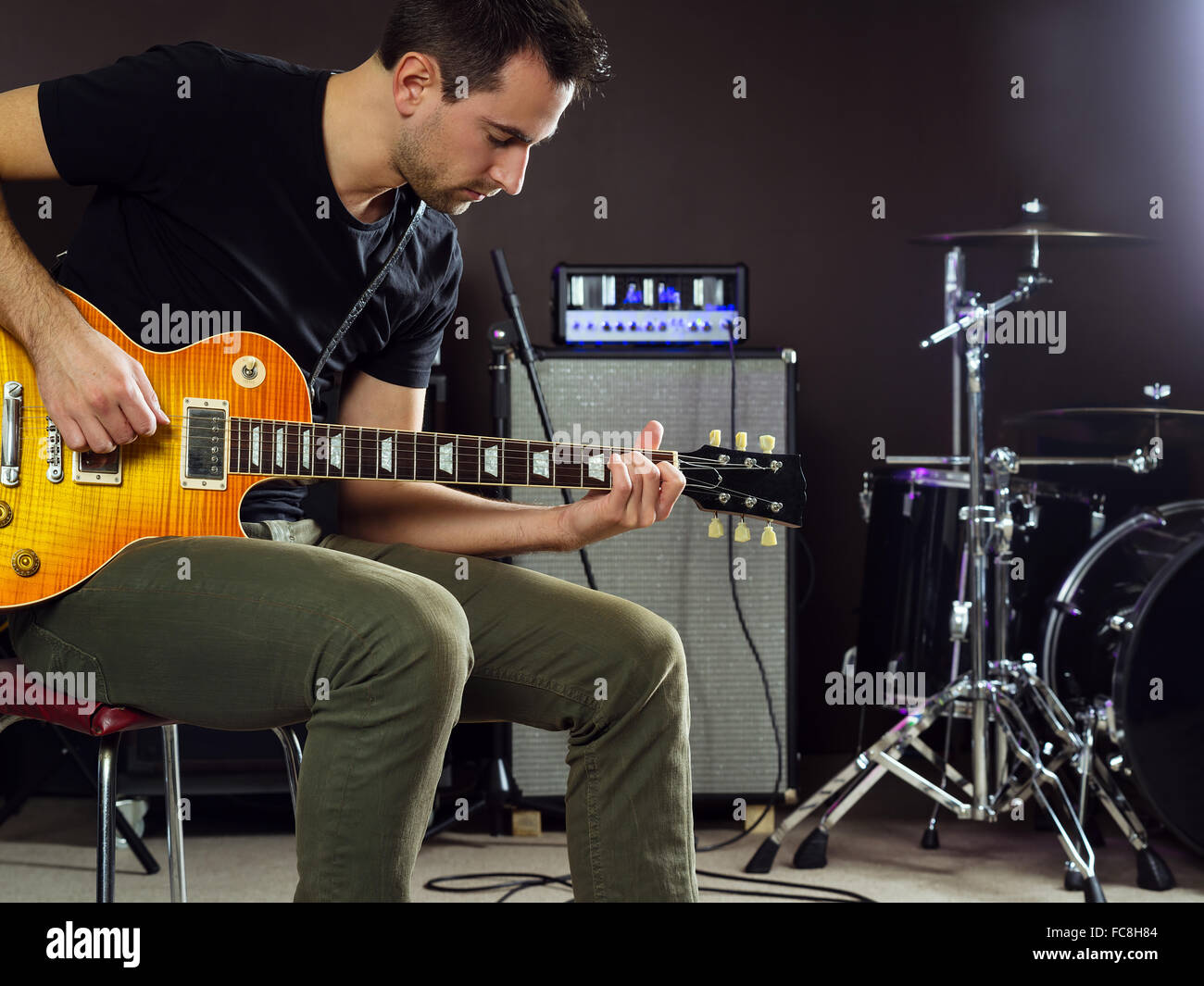 Photo of a man in his late 20's sitting on stage playing guitar. Stock Photo