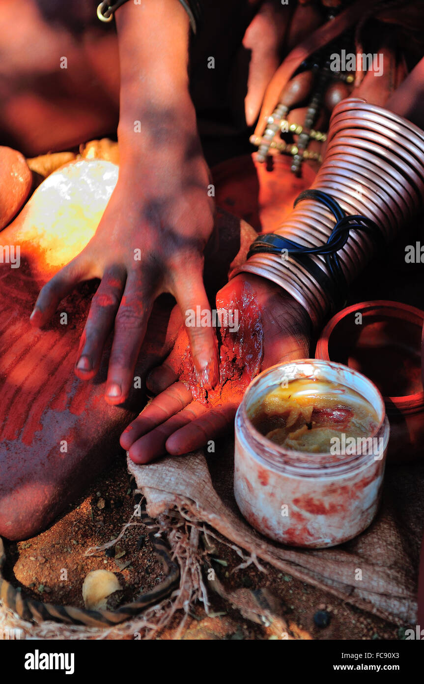 Himba woman mixing red ochre with petroleum jelly to apply to body. Traditionally it was mixed with animal fat. Stock Photo
