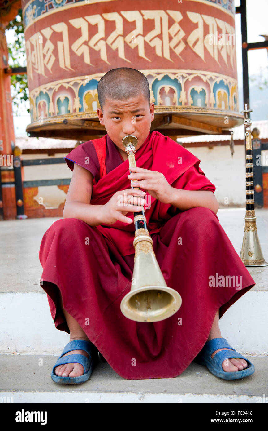 Monk playing lingum trumpet in front of a prayer wheel, Punakha, Bhutan, Asia Stock Photo
