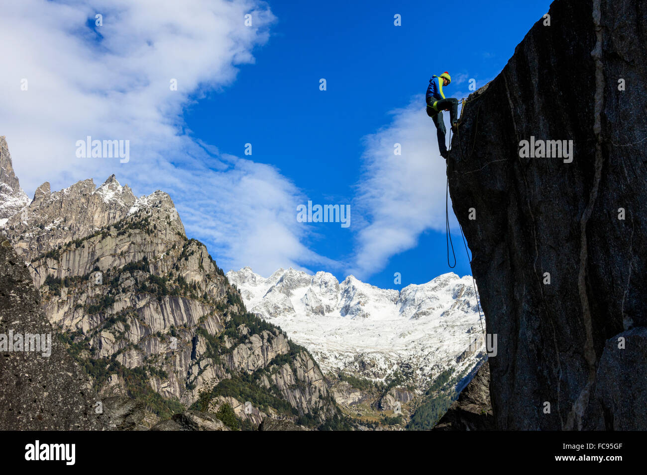 Climber on steep rock face in the background blue sky and snowy peaks of the Alps, Masino Valley, Valtellina, Lombardy, Italy Stock Photo