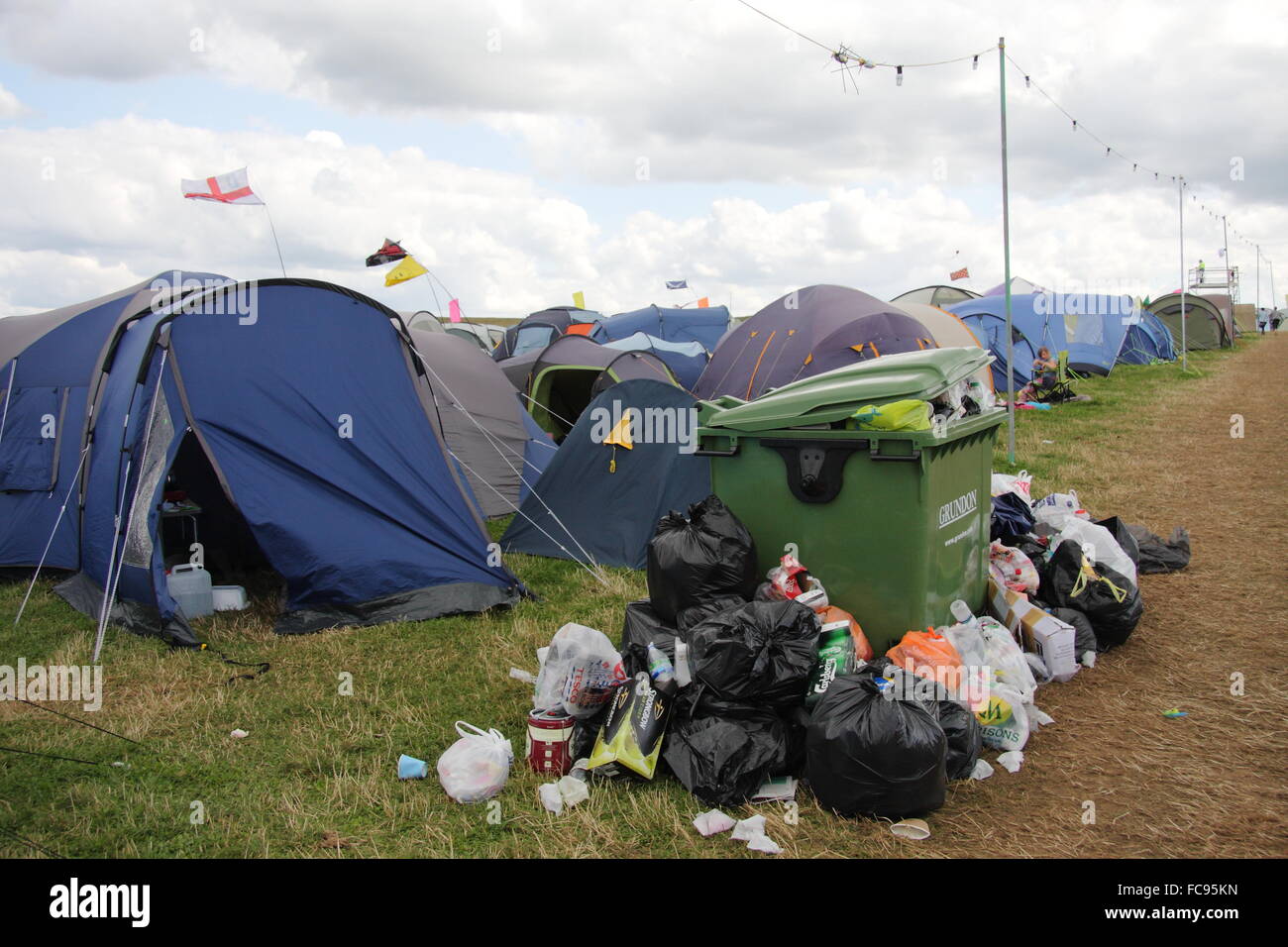 Rubbish surrounds a bin by festival goers' tents in a camping field at the Y Not music festival in the Peak District, UK Stock Photo