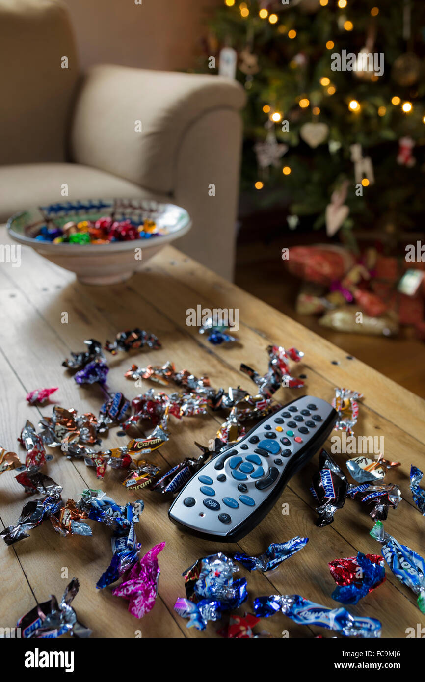 TV remote control surrounded by sweet wrappers at Christmas. Stock Photo