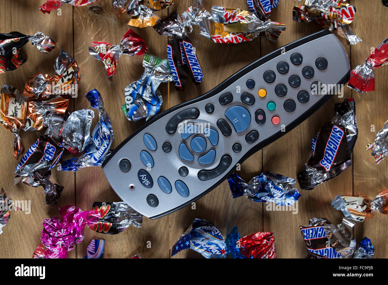 TV remote control surrounded by sweet wrappers at Christmas. Stock Photo