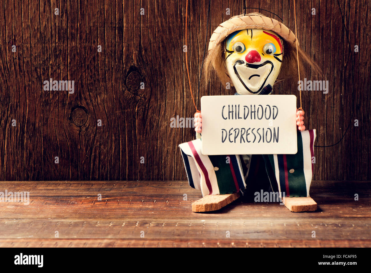 closeup of an old marionette with its face painted as a sad clown holding a signboard with the text childhood depression Stock Photo