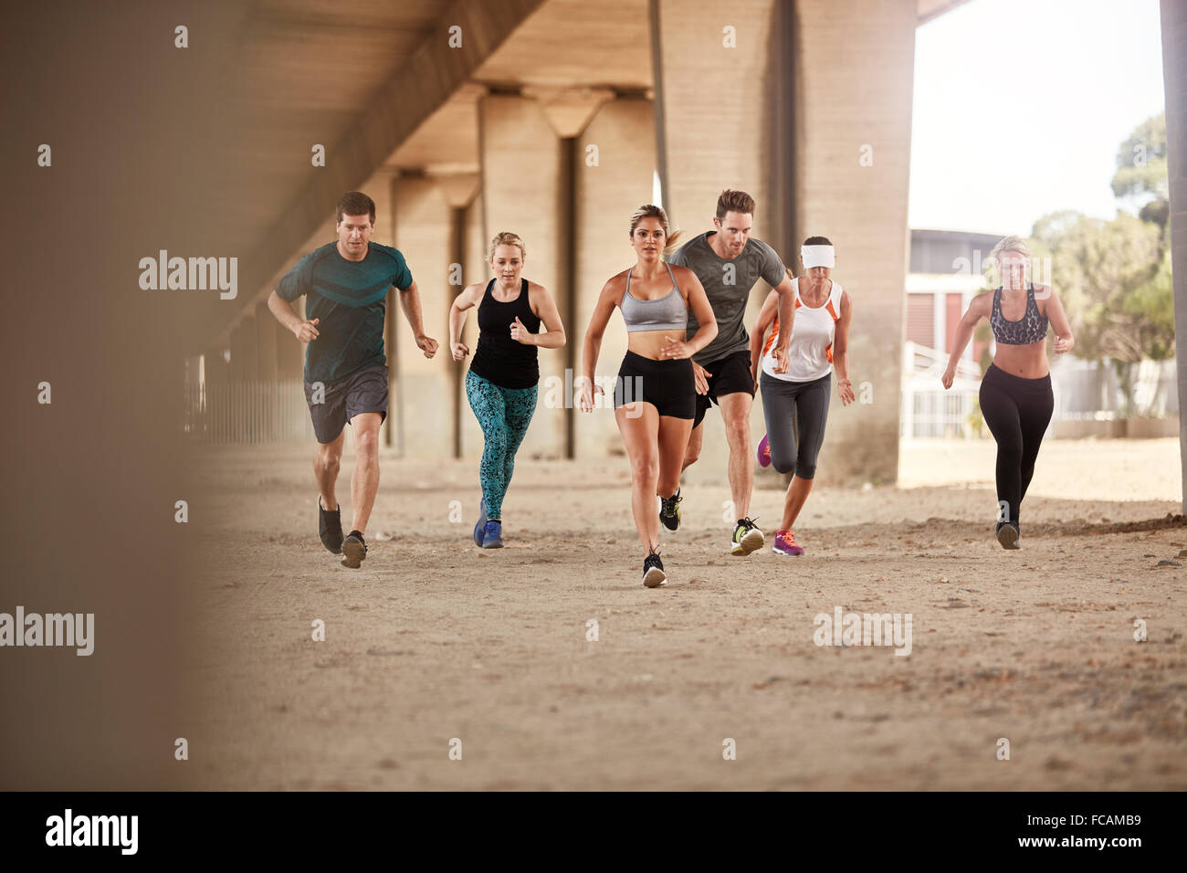 Portrait of group of runners in fitness clothing running under a bridge