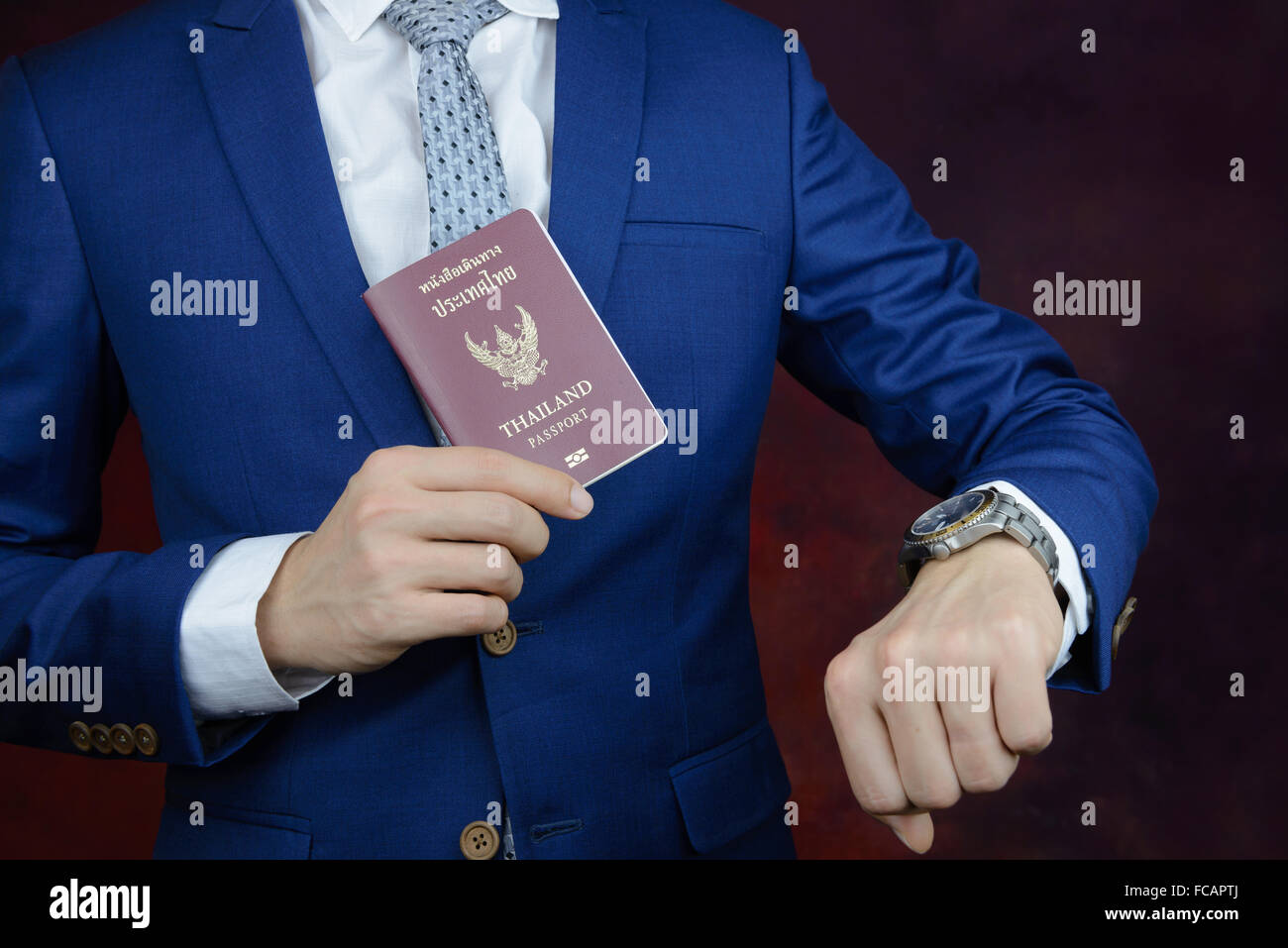 businessman in blue suit checking time on watch, showing passport Stock Photo