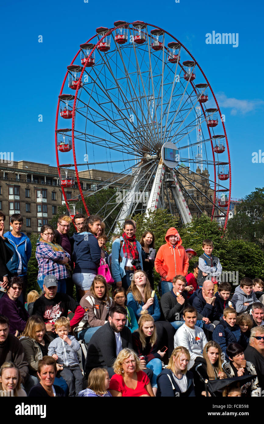A crowd at the Edinburgh Fringe Festival watch a street performer while the Festival Wheel spins in the background. Stock Photo