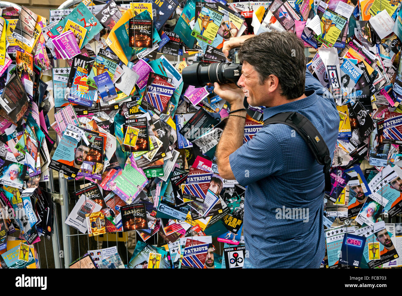 A male photographer taking a photograph against a backdrop of fliers during the Edinburgh Fringe Festival. Stock Photo