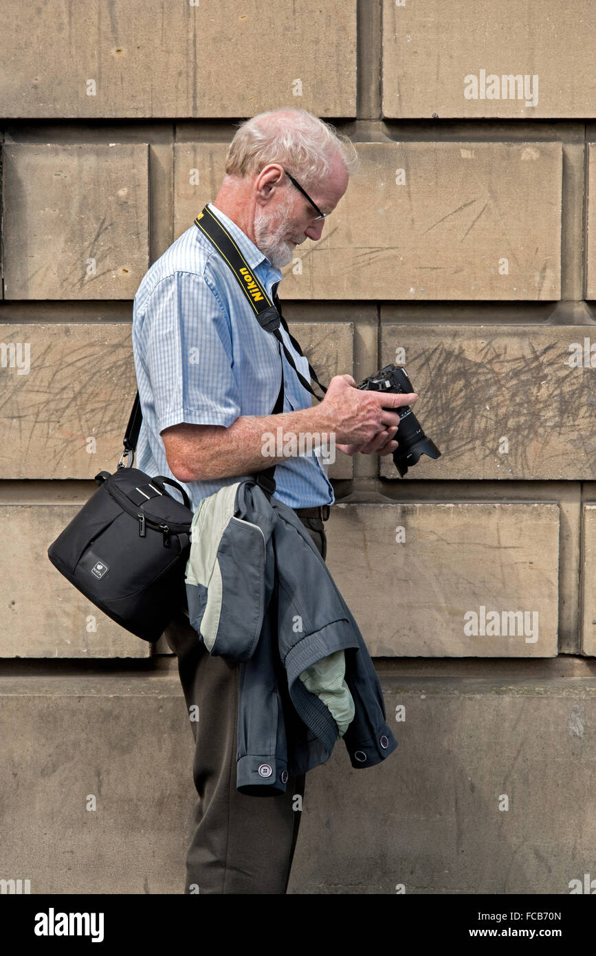 A middle-aged photographer holding a Nikon camera checking his photographs in the rear viewfinder of his camera. Stock Photo