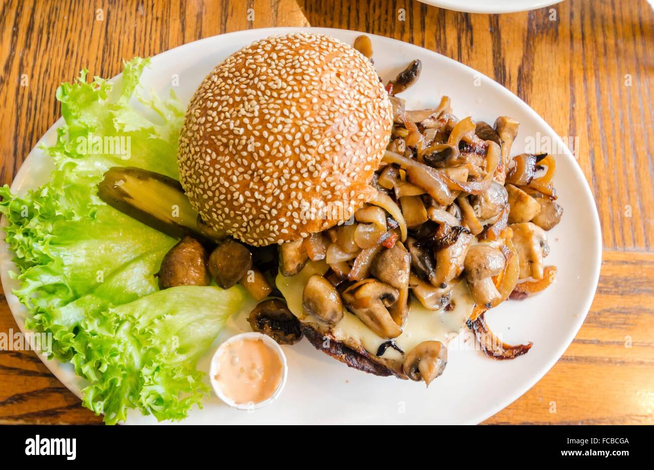 A dish with a hamburger with sauteed mushrooms on top, sesame bun bread