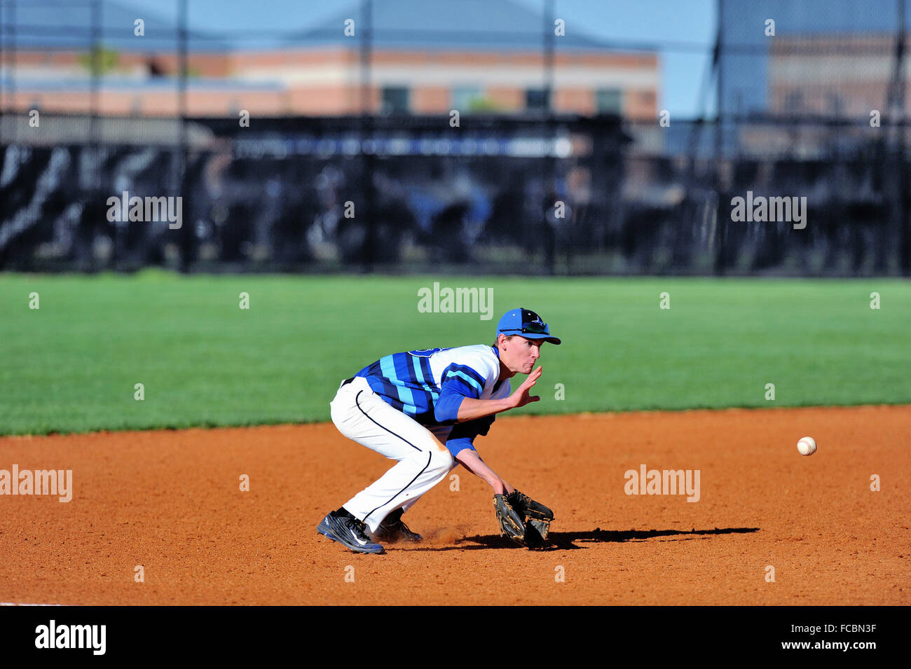 A high school third baseman positioned to field a ground ball during a