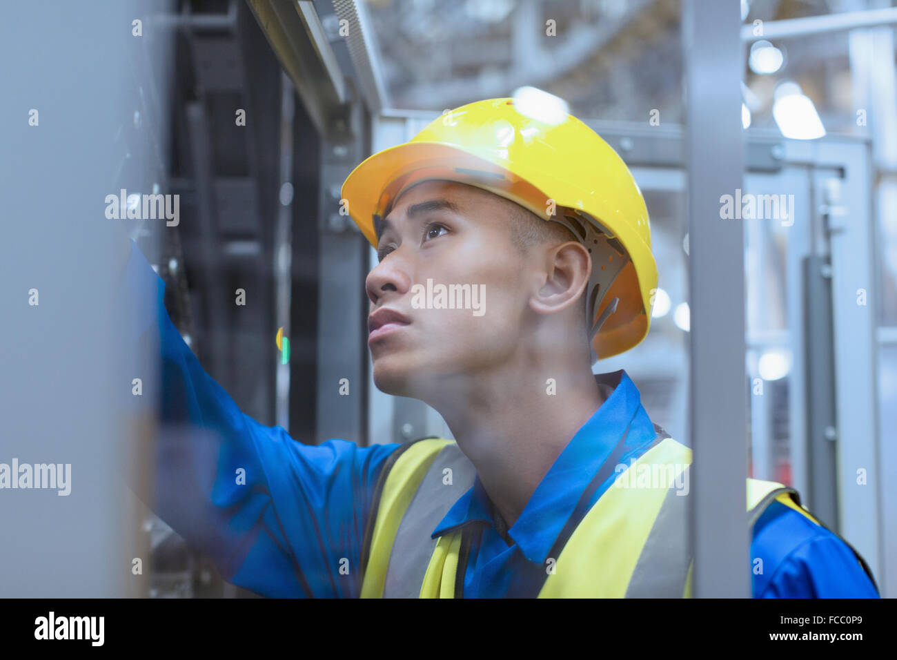 Worker in hard-hat examining machinery in factory Stock Photo