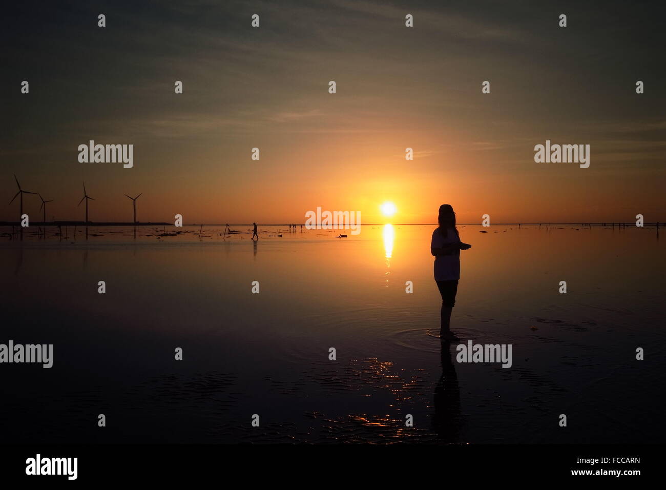 Silhouette Woman Standing On Beach At Sunset Stock Photo