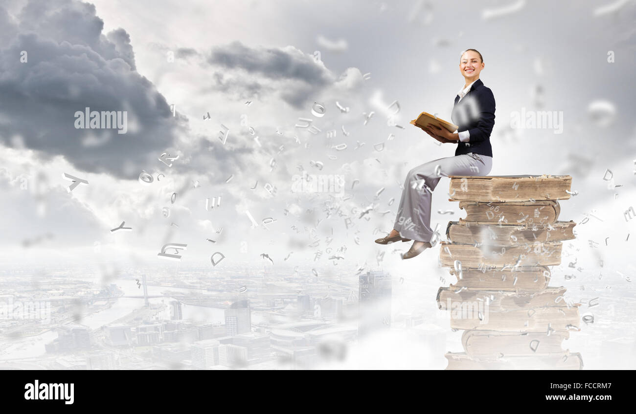 Young attractive woman sitting on pile of books and reading Stock Photo ...