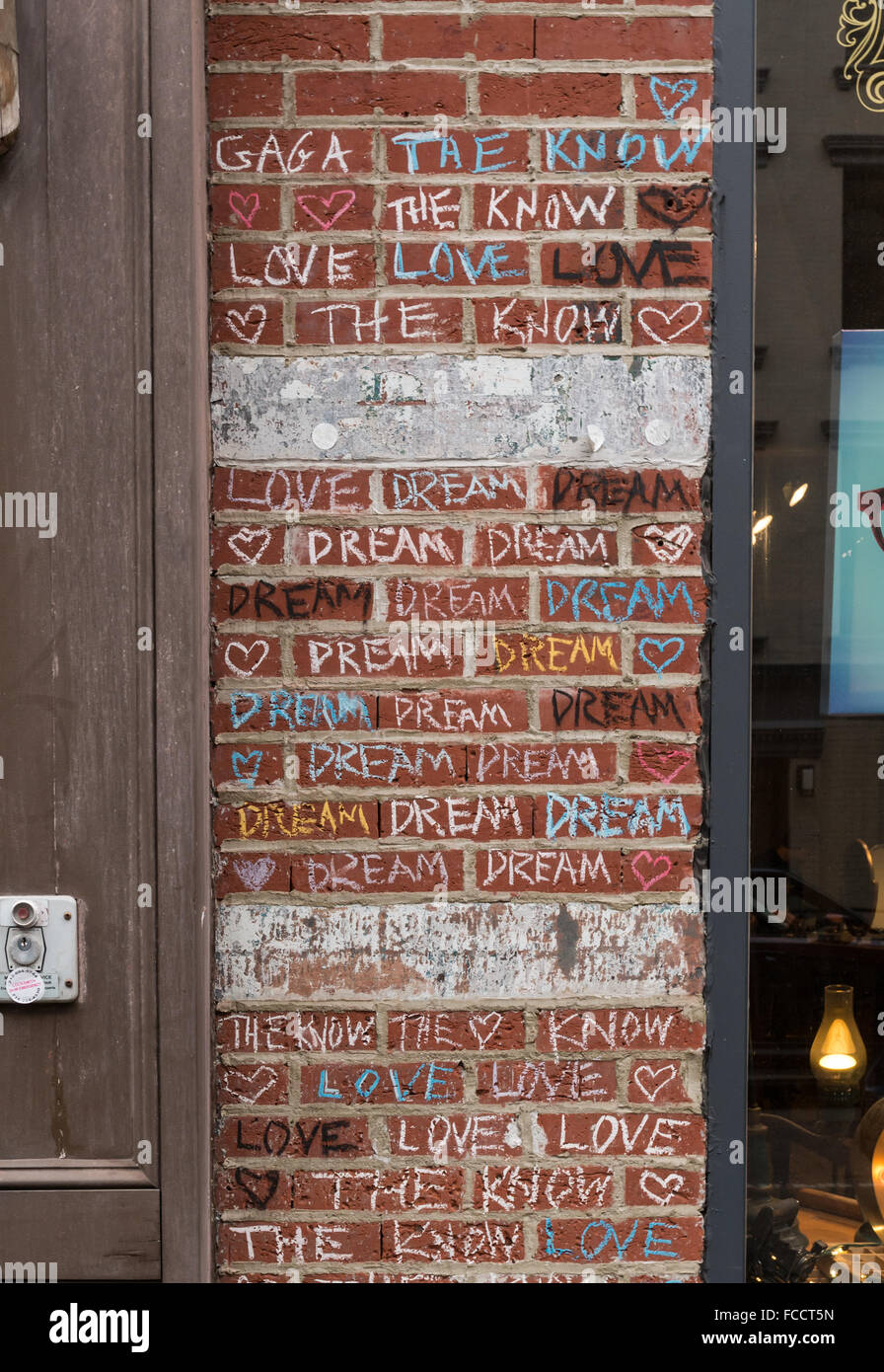 Coloured chalk graffiti on a red brick wall with the words love, dream, and the know on the outside of a shop. Stock Photo