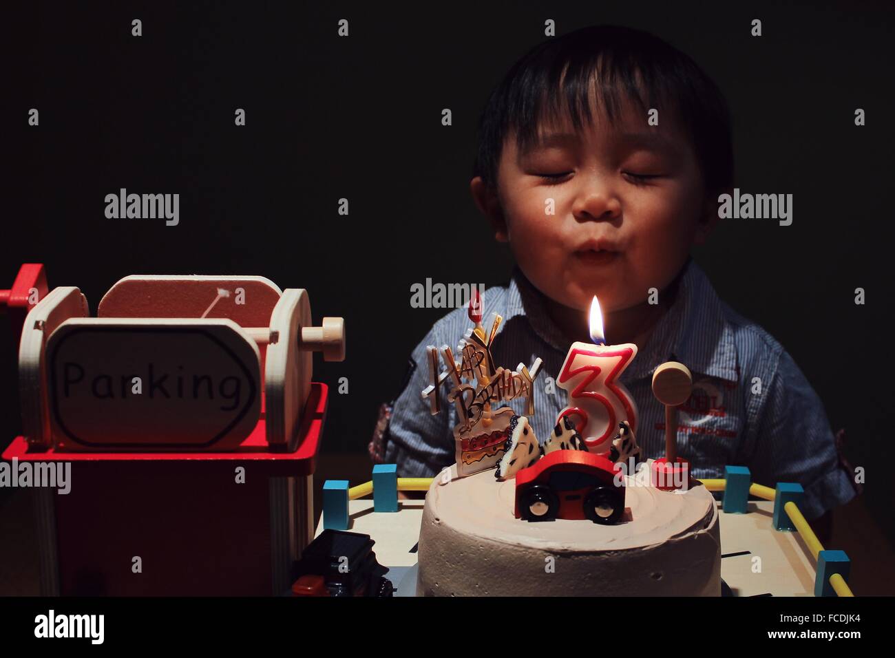 Cute Boy With Eye Closed Blowing Birthday Candle On Cake In Darkroom Stock Photo