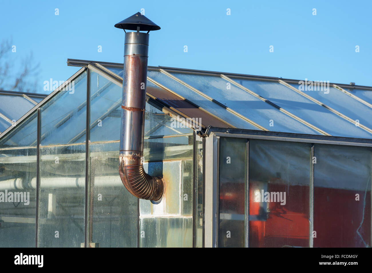 A small metal chimney stick out from a greenhouse with a heater inside. Stock Photo