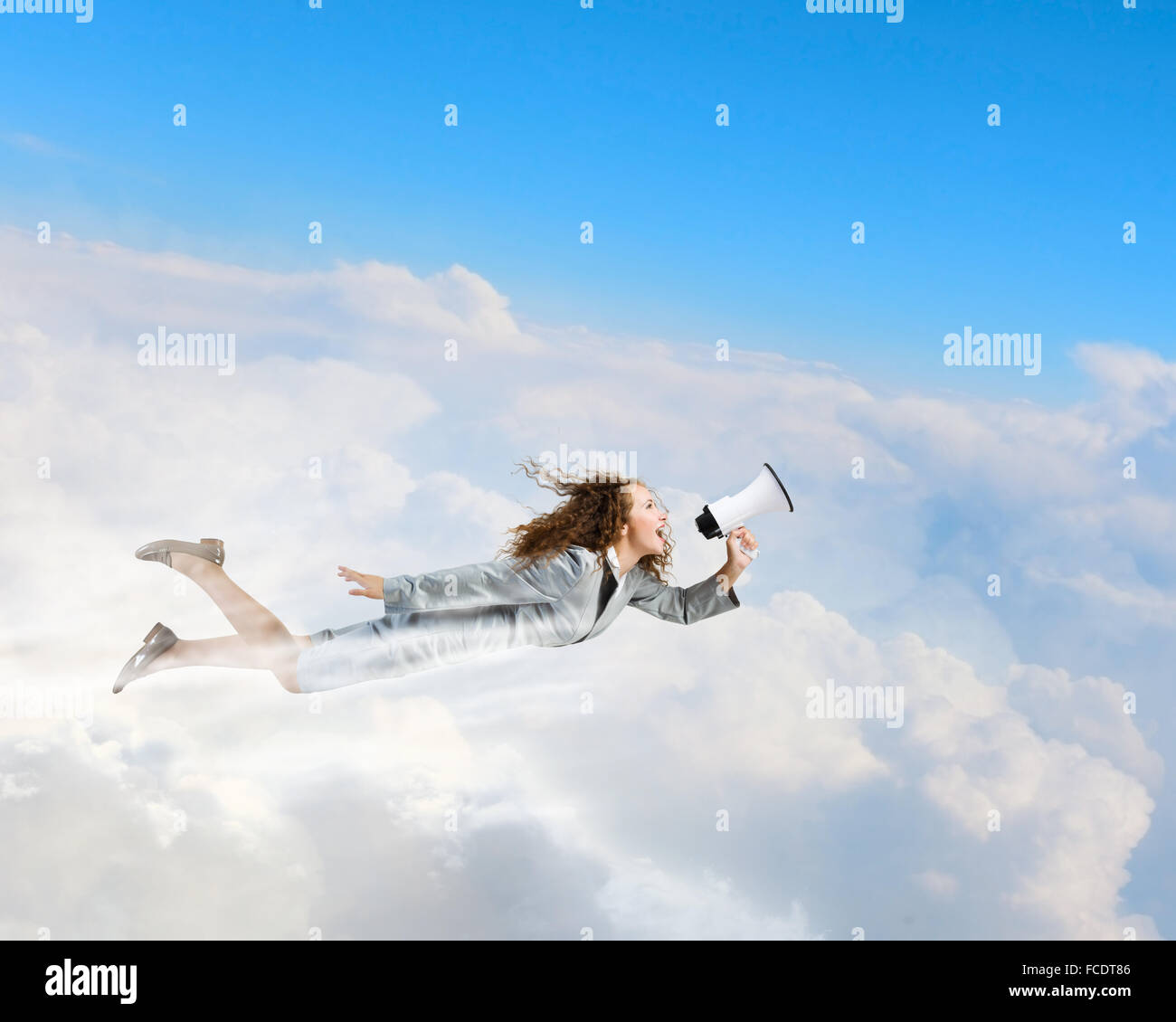 Young businesswoman with megaphone flying high in sky Stock Photo