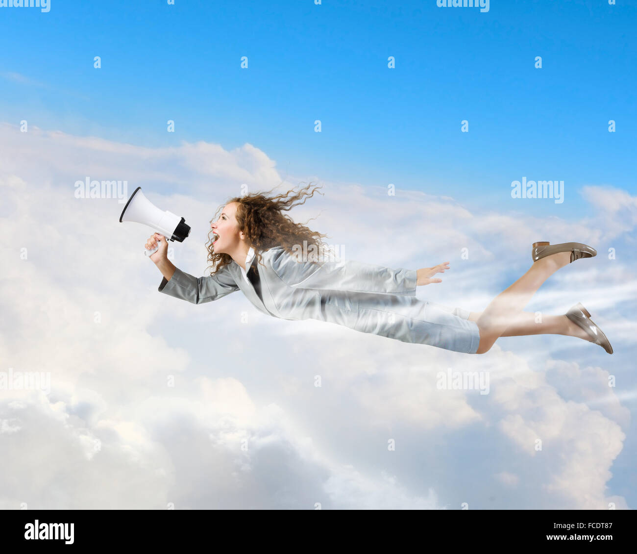 Young businesswoman with megaphone flying high in sky Stock Photo