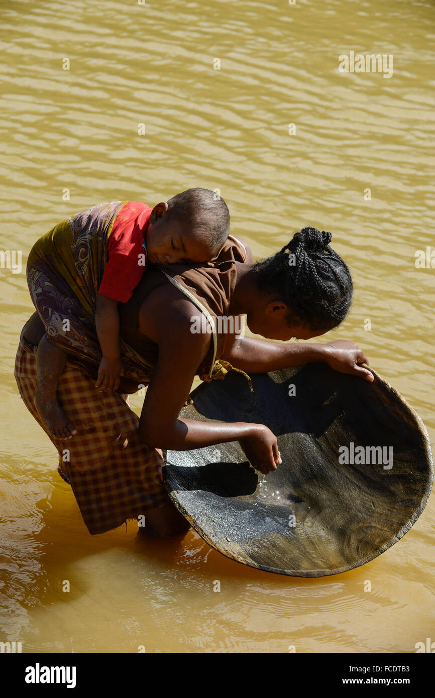 MADAGASCAR, region Manajary, town Vohilava, small scale gold mining, women panning for gold at river ANDRANGARANGA, mother carry her child on the back during the work / MADAGASKAR Mananjary, Vohilava, kleingewerblicher Goldabbau, Frauen waschen Gold am Fluss ANDRANGARANGA, Mutter traegt ihr Kind bei der Arbeit auf dem Ruecken Stock Photo