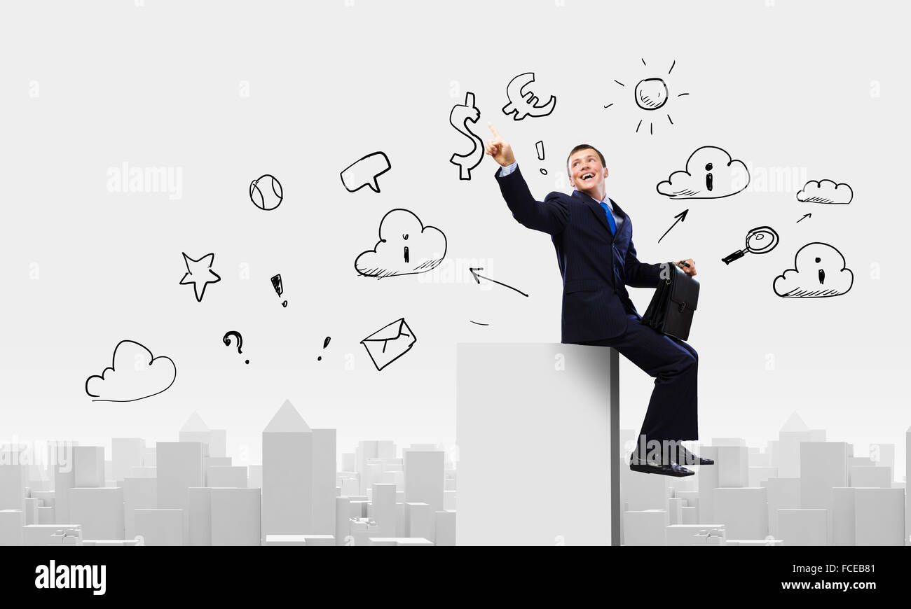 Young businessman with suitcase sitting on roof of building Stock Photo ...