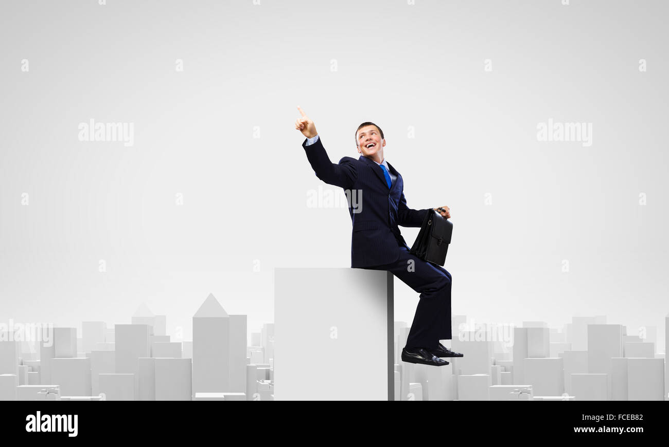 Young businessman with suitcase sitting on roof of building Stock Photo ...