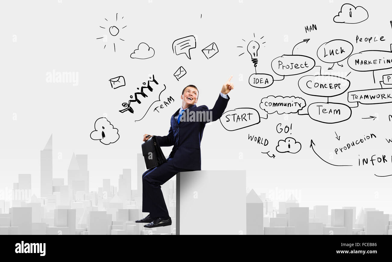 Young businessman with suitcase sitting on roof of building Stock Photo ...