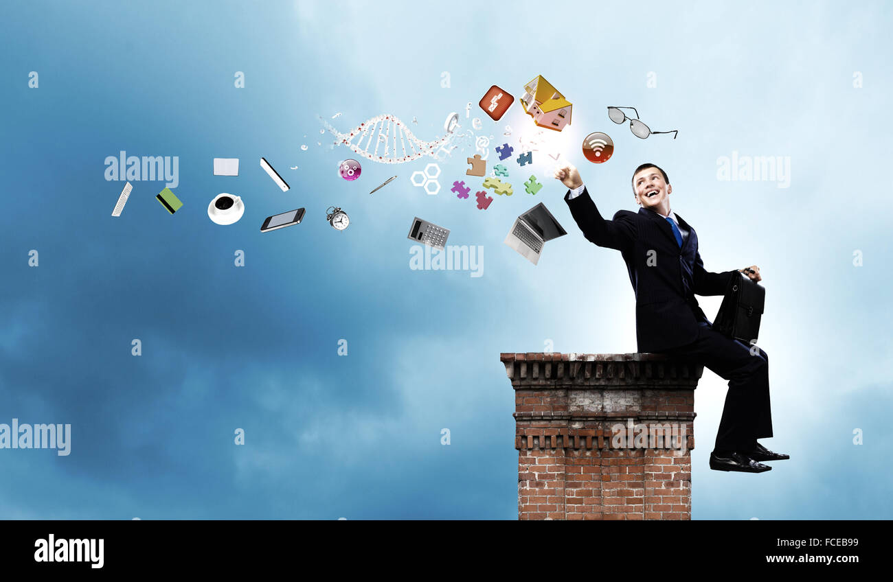 Young businessman with suitcase sitting on roof of building Stock Photo ...