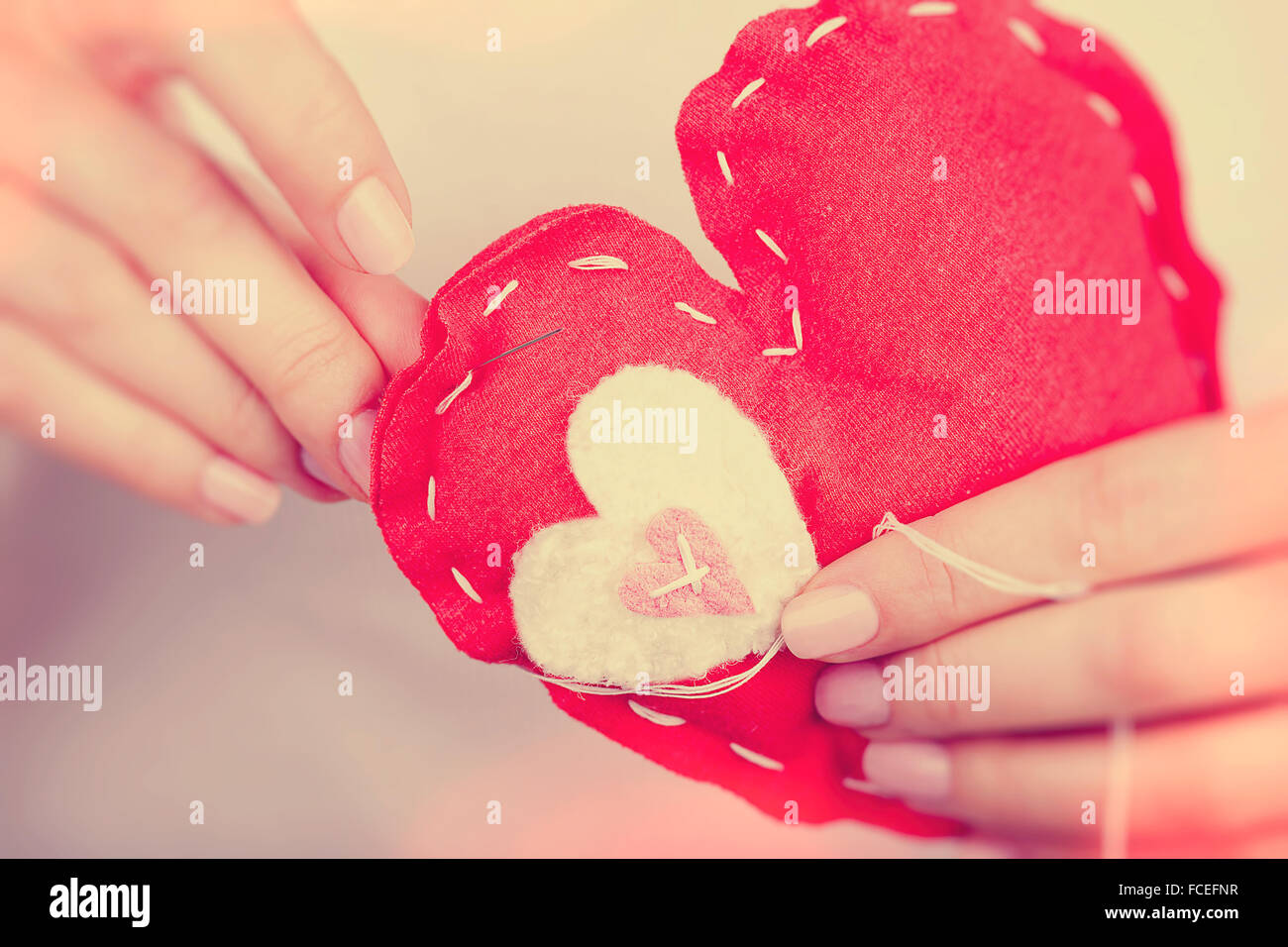 Woman sews red heart shaped toy by needle, body part, conceptual symbol of love and soul pain treatment, happy Valentine day Stock Photo