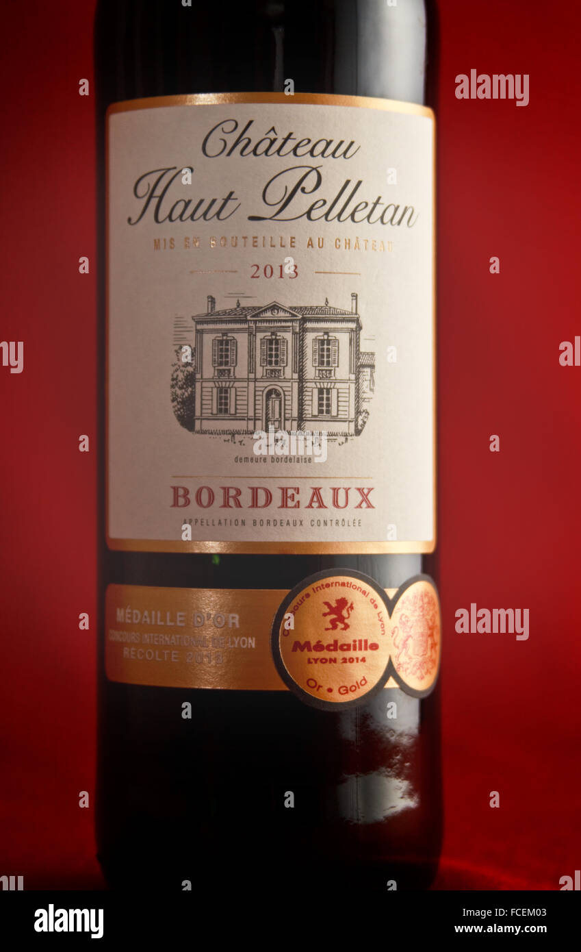 A single bottle of French Bordeaux wine on a crimson base and backdrop