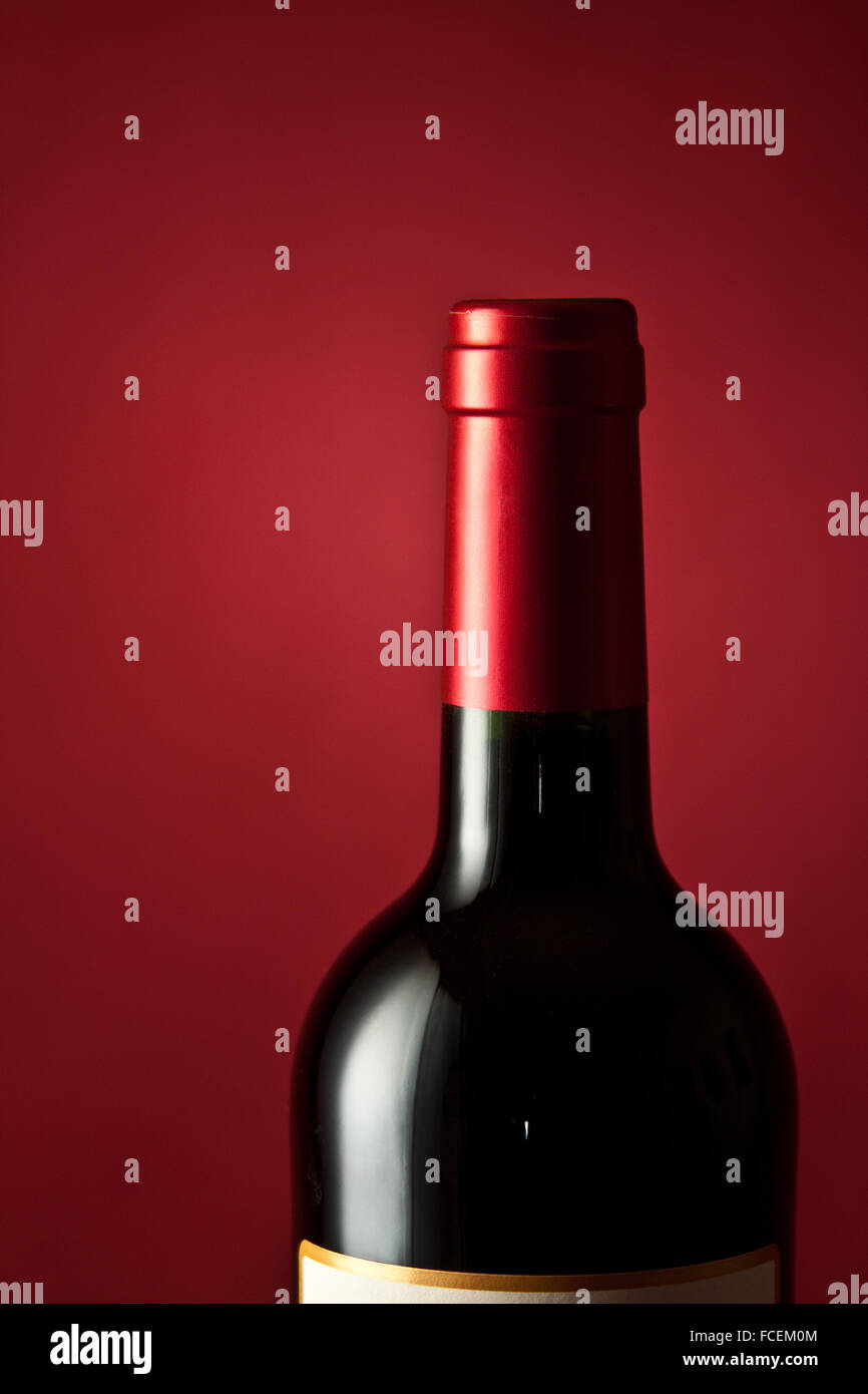 A single bottle of French Bordeaux wine on a crimson base and backdrop. Stock Photo