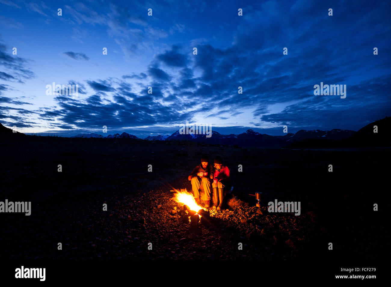 Two campers huddle together at a campfire in Glacier Bay National Park, Alaska. Stock Photo