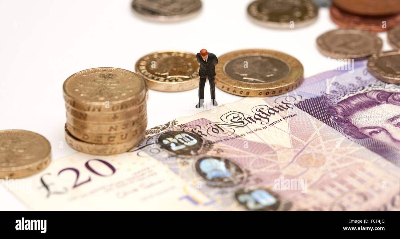 A Miniature male figurine in a suit standing next to pound coins and a twenty pound note showing the words Bank of England Stock Photo