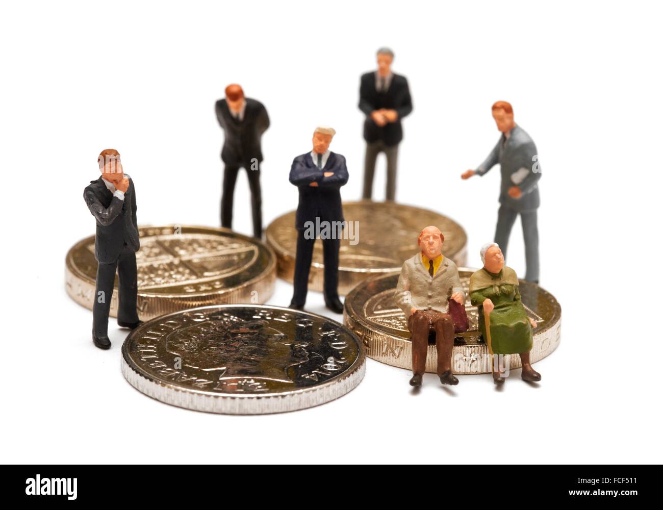 A Miniature pensioner couple sitting on british coins surrounded by financial advisor's in suits concept. Stock Photo
