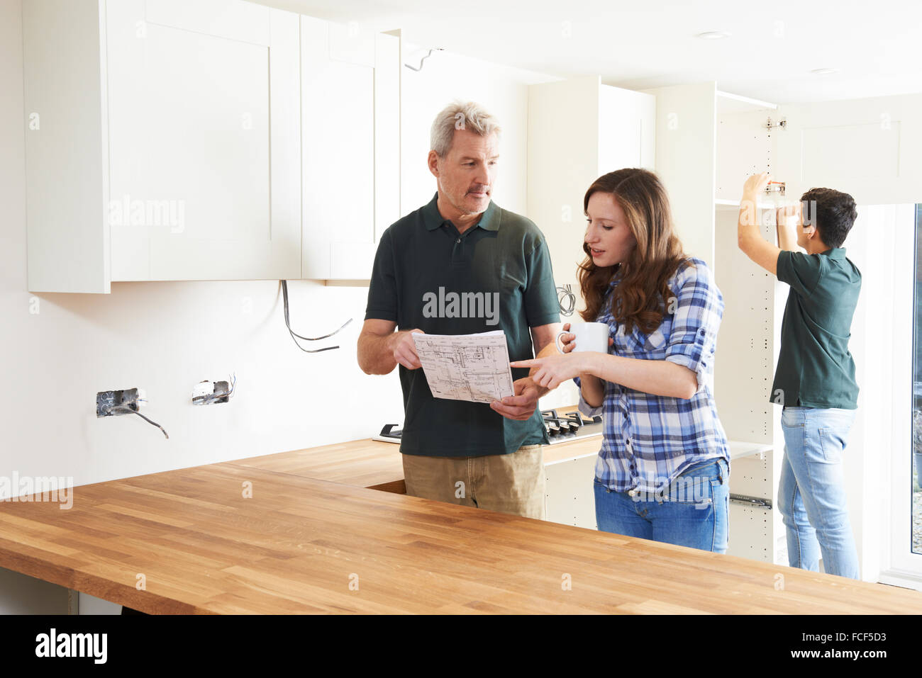 Woman With Carpenter Looking At Plans For New Kitchen Stock Photo